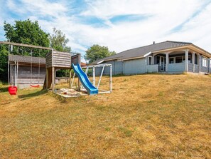 A residential backyard with a wooden play structure, a blue slide, and a covered porch. - 4 Star Holiday Home in Glesborg (Glesborg)