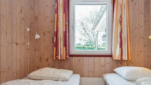 Quarto com duas camas, paredes de madeira, janela com cortinas e um abajur.