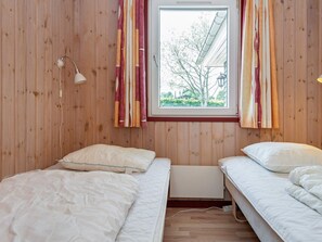 A room with two beds, wooden walls, a window with curtains, and a lamp. - 4 Star Holiday Home in Glesborg (Glesborg)