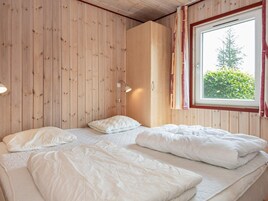 Ein Zimmer mit Holzwandverkleidung, einem Bett mit weißer Bettwäsche, einer Nachttischlampe und einem Fenster mit Vorhängen.