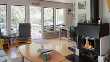 Ein gemütliches Wohnzimmer mit Kamin, Fernseher und einem großen Fenster mit Blick ins Freie.