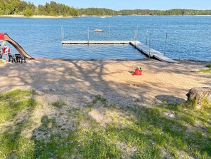 A lakeside beach with a wooden dock extending into the water, a red bucket, and a pair of chairs on the sand. - 4 Star Holiday Home in Norrtalje (Norrtälje)