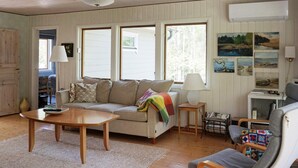 A cozy living room with a sofa, a coffee table, and a chair. There are windows, a lamp, and wall art. - 4 Star Holiday Home in Norrtalje (Norrtälje)