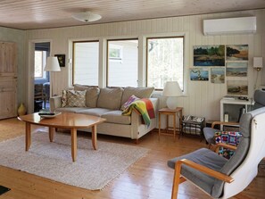 A cozy living room with a sofa, a coffee table, and a chair. There are windows, a lamp, and wall art. - 4 Star Holiday Home in Norrtalje (Norrtälje)