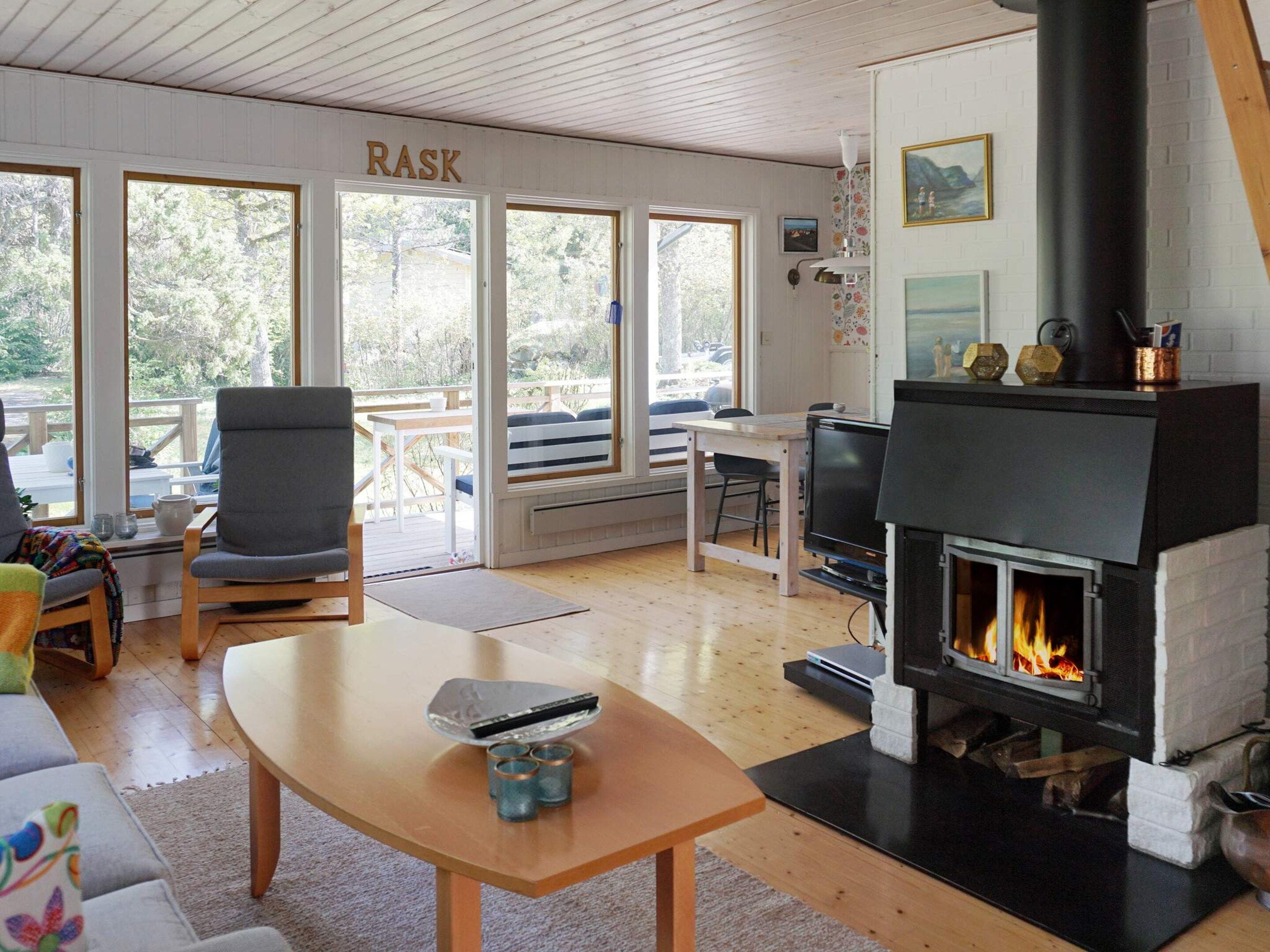 A cozy living room with a fireplace, a television, and a large window overlooking a deck.