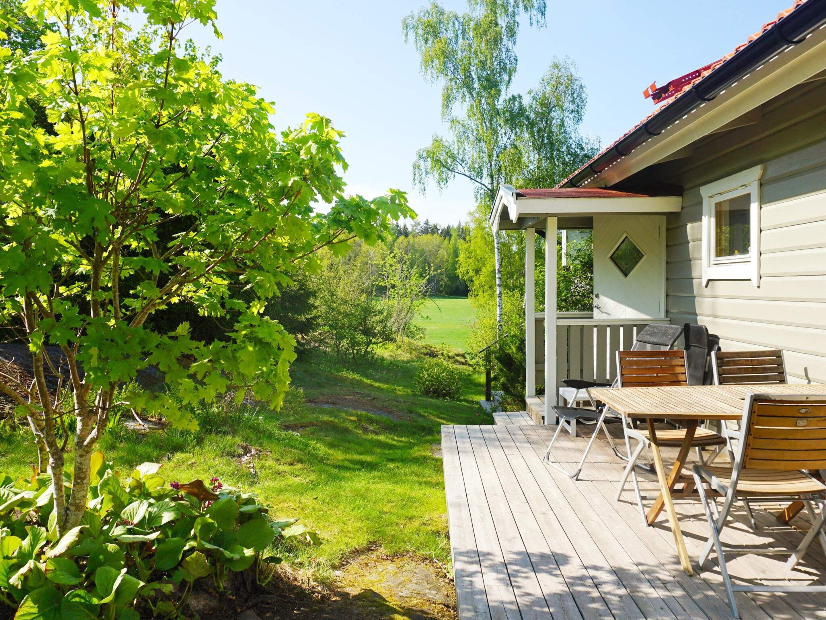 Eine Holzterrasse mit Gartenmöbeln, eine überdachte Veranda und Blick auf eine grüne Landschaft.