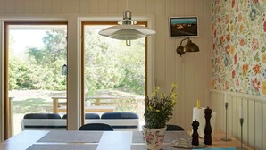 A dining area with a table, chairs, a hanging light fixture, a potted plant, and a wall with floral wallpaper. - 4 Star Holiday Home in Norrtalje (Norrtälje)