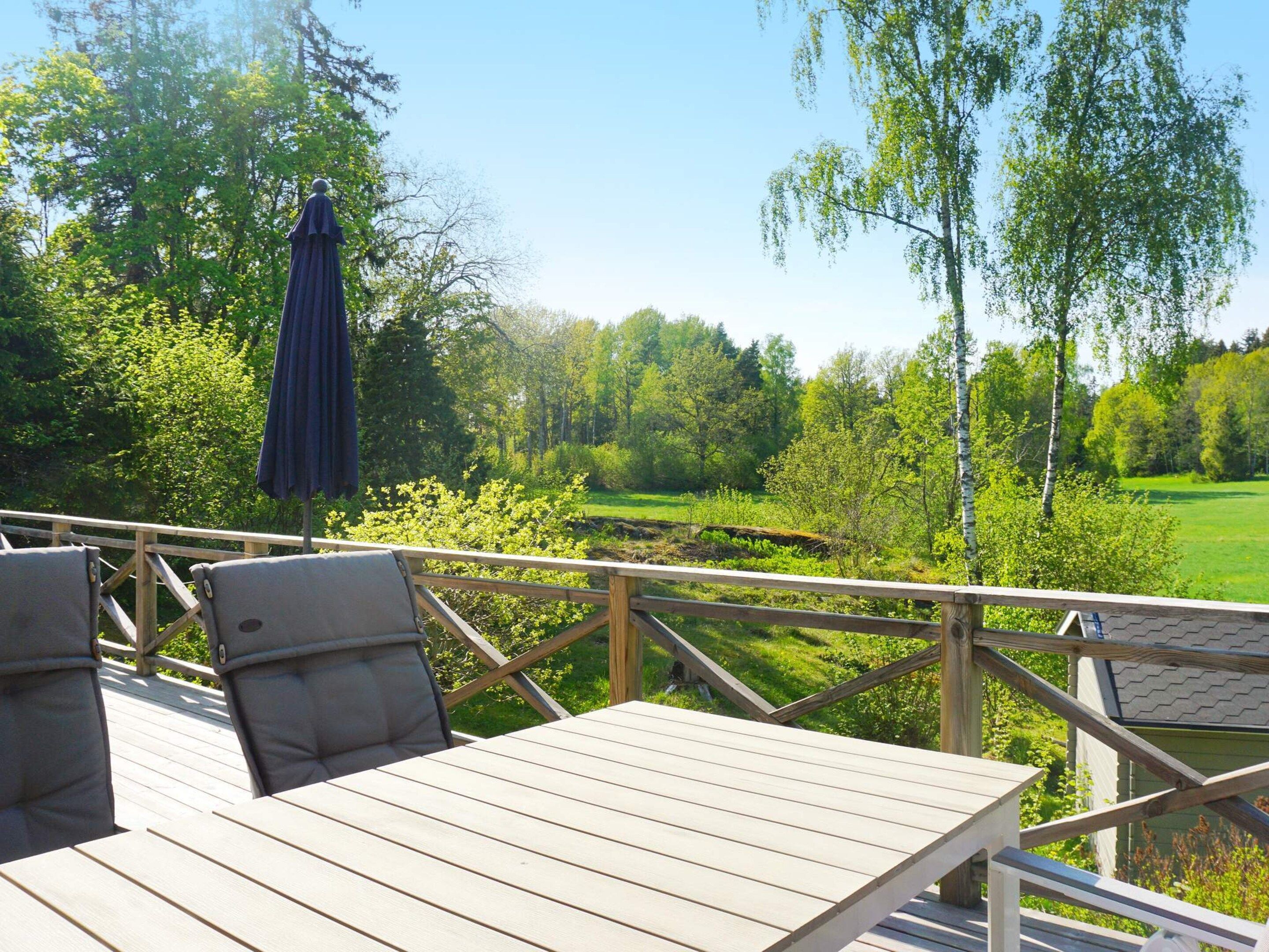 A wooden deck with a table and chairs, overlooking a green landscape with trees and a clear sky.