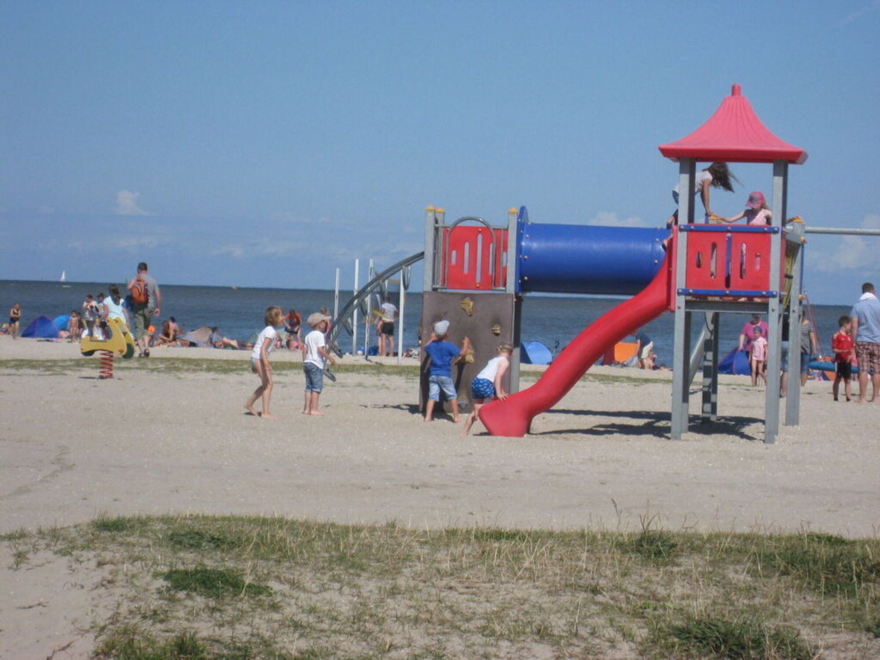 A beach playground with a red slide and a blue climbing structure.