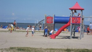 A beach playground with a red slide and a blue climbing structure. - North Sea House Schillig (Wangerland)
