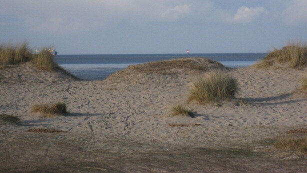 A sandy beach with dunes and a distant lighthouse. - North Sea House Schillig (Wangerland)