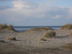 Une plage de sable avec des dunes et un phare situé au loin.