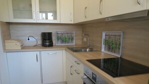A modern kitchen with white cabinets, a stainless steel sink, a built-in oven, and a black induction cooktop. - North Sea House Schillig (Wangerland)