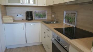A modern kitchen with white cabinets, a stainless steel sink, a built-in oven, and a black induction cooktop.