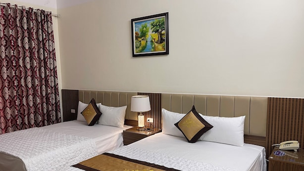 A hotel room with two beds, a painting on the wall, a nightstand with a lamp, and a wooden desk with a telephone. - Phuoc Thinh Hostel HN - by Bay Luxury (Hanoi)