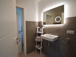 Un baño moderno con un lavamanos blanco, un espejo con luz circular y un perchero para toallas.