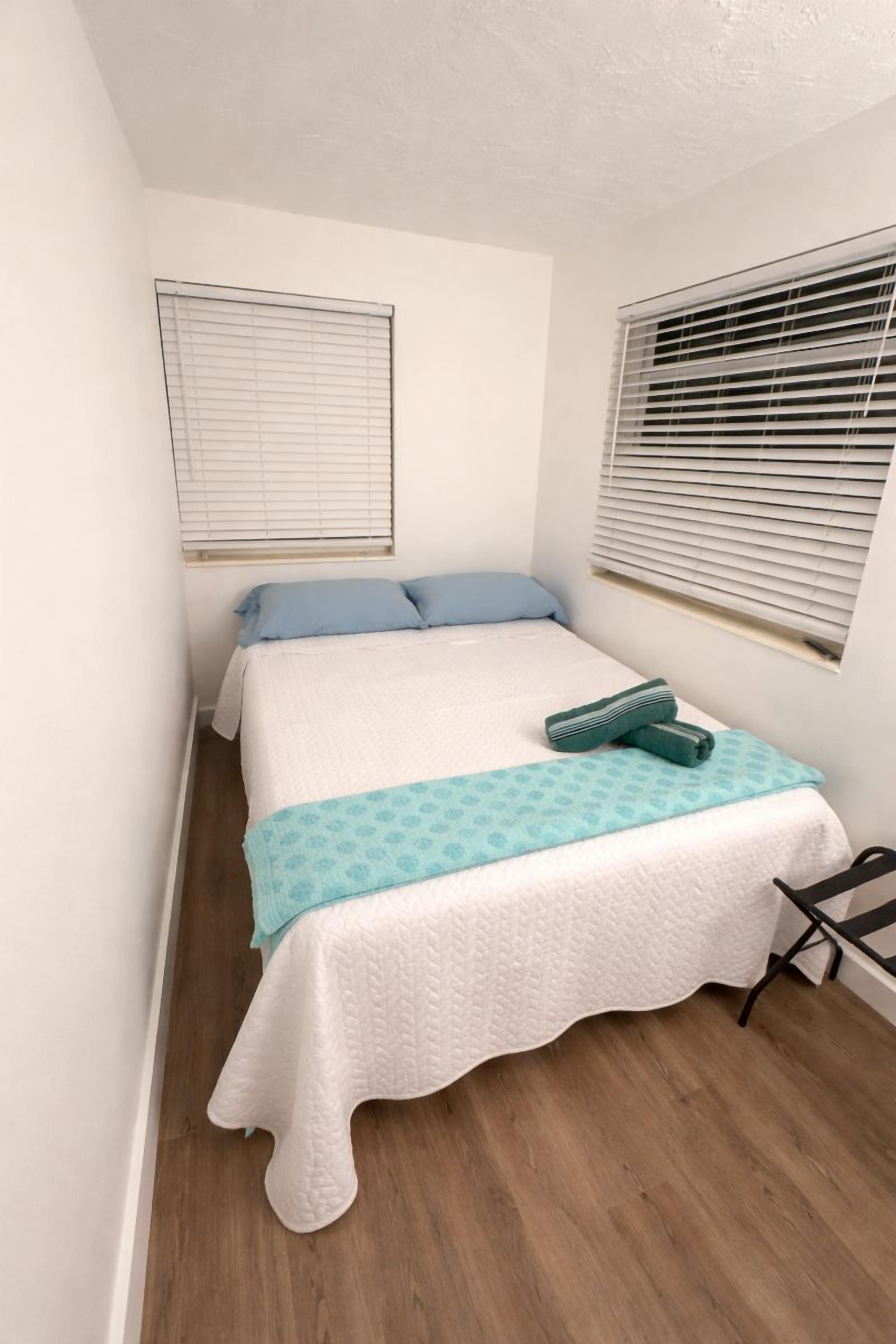 A bedroom with a bed, a window with blinds, and a wooden floor.