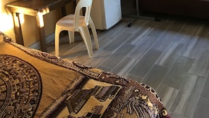 Une pièce de taille modeste comprenant un lit, un bureau avec une chaise, un réfrigérateur, un ventilateur et un canapé.