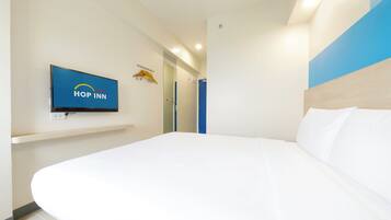 A modern hotel room with a large bed, a mounted television displaying the 'Hop Inn' logo, and a blue accent wall.