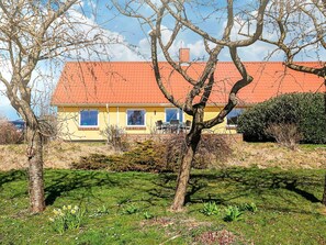 A yellow house with a red roof, surrounded by trees and a grassy lawn. - 4 Person Holiday Home in Ostervra (Østervrå)