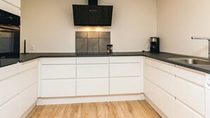 Una cocina moderna con armarios blancos, una campana extractora negra y un lavamanos de acero inoxidable.