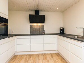 A modern kitchen with white cabinetry, a black range hood, and a stainless steel sink. - 4 Person Holiday Home in Ostervra (Østervrå)