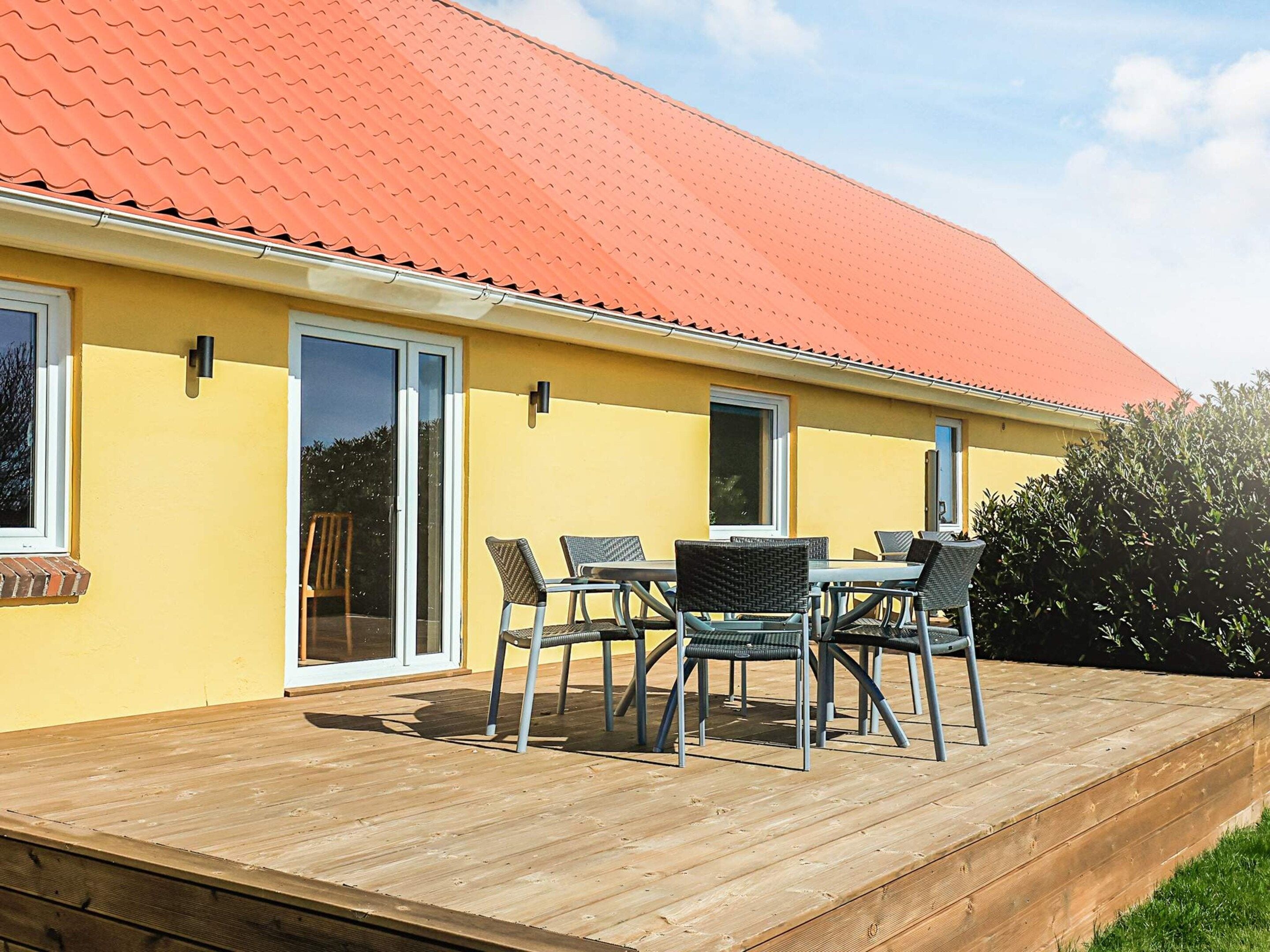 A yellow building with a red roof, a wooden deck, and outdoor furniture.
