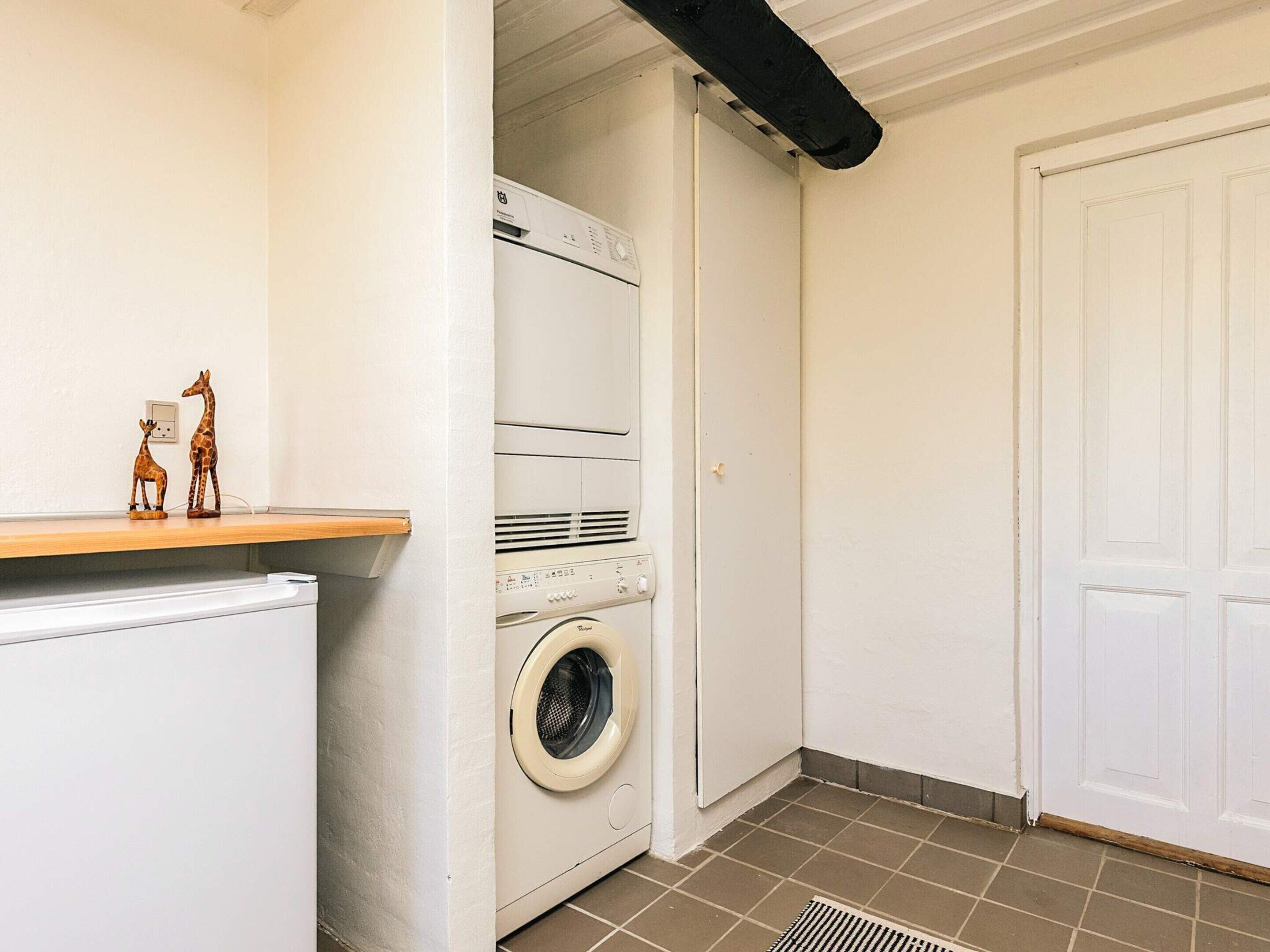 A compact laundry room with a washing machine and dryer, a small shelf with decorative items, and a white door.