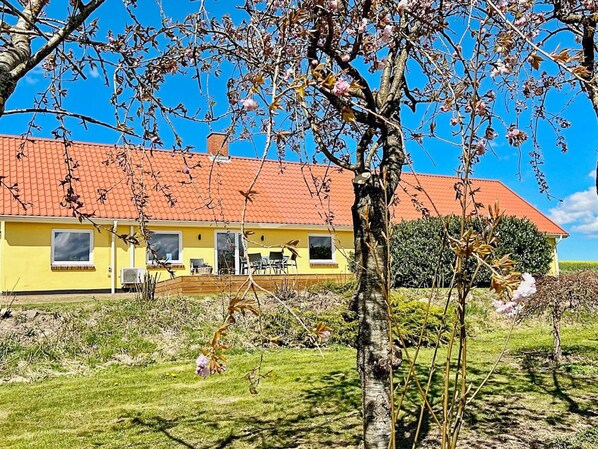 A yellow building with a red roof, a visible window, and a tree in the foreground. - 4 Person Holiday Home in Ostervra (Østervrå)