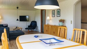 Un salón moderno con una mesa de comedor, sillas, un sillón de cuero negro, un televisor y una pared de ladrillo blanco.