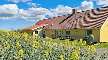 Um edifício amarelo com telhado de telhas vermelhas, rodeado por um campo de flores amarelas.