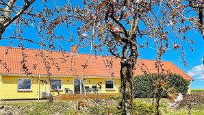 A yellow building with a red roof, a covered patio, and a grassy area with trees. - 4 Person Holiday Home in Ostervra (Østervrå)
