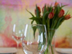 A clear glass table setting with a vase of tulips in the background.