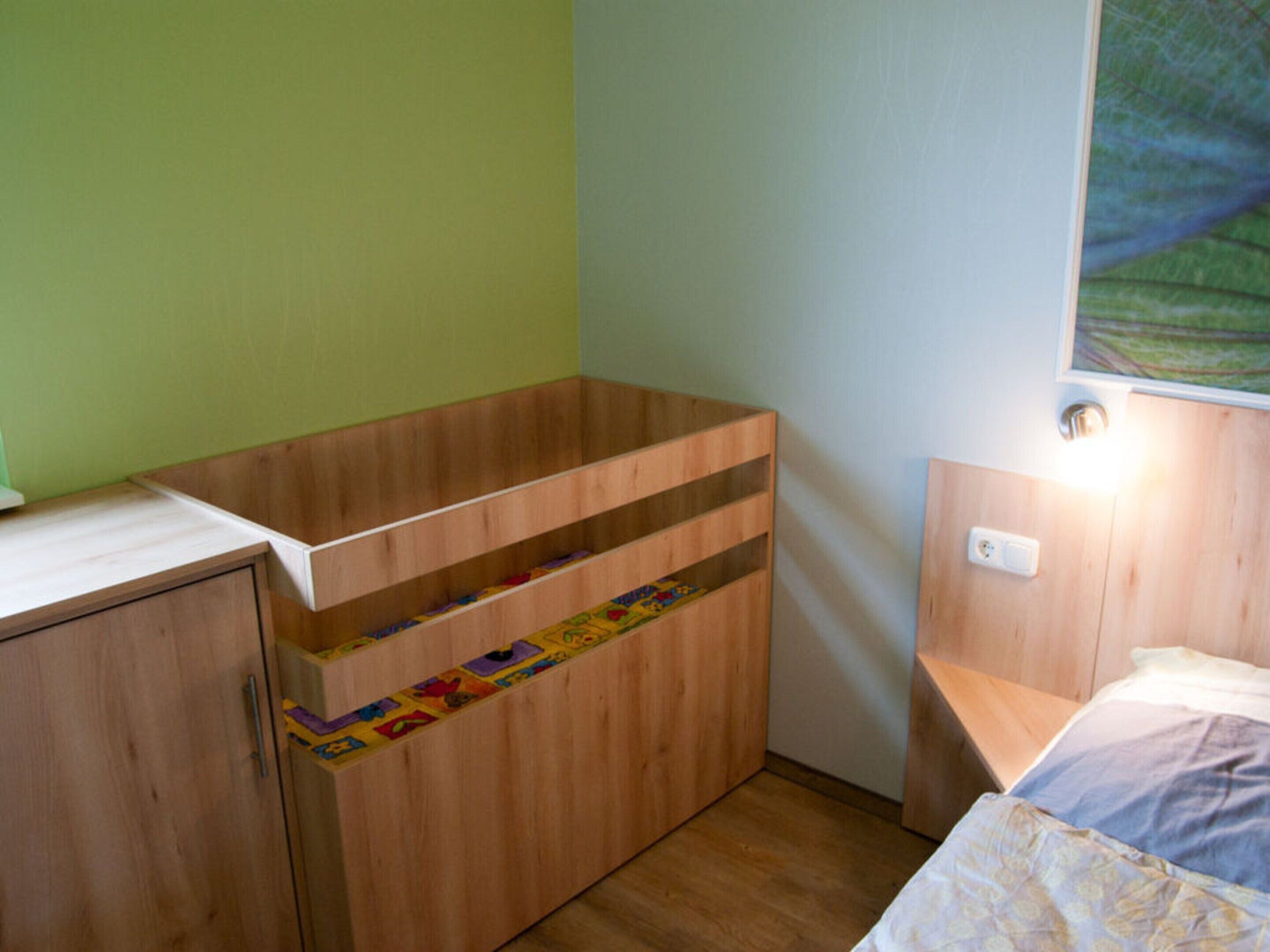 Une petite pièce, de taille modeste, comprenant un bureau en bois, un lit et une lampe fixée au mur.