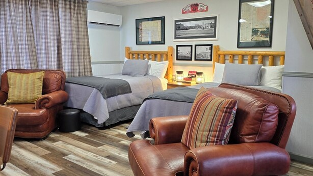 Habitación de hotel con dos camas, cabecero de madera, sillón de cuero, una mesita con lámpara y aire acondicionado de pared.