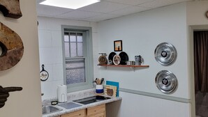 Una cocina con paredes de azulejos blancos, una ventana, un lavamanos y una encimera con diversos utensilios de cocina.
