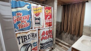 Un baño con cortina de ducha decorada con anuncios de temática automotriz, un lavamanos y un espejo.