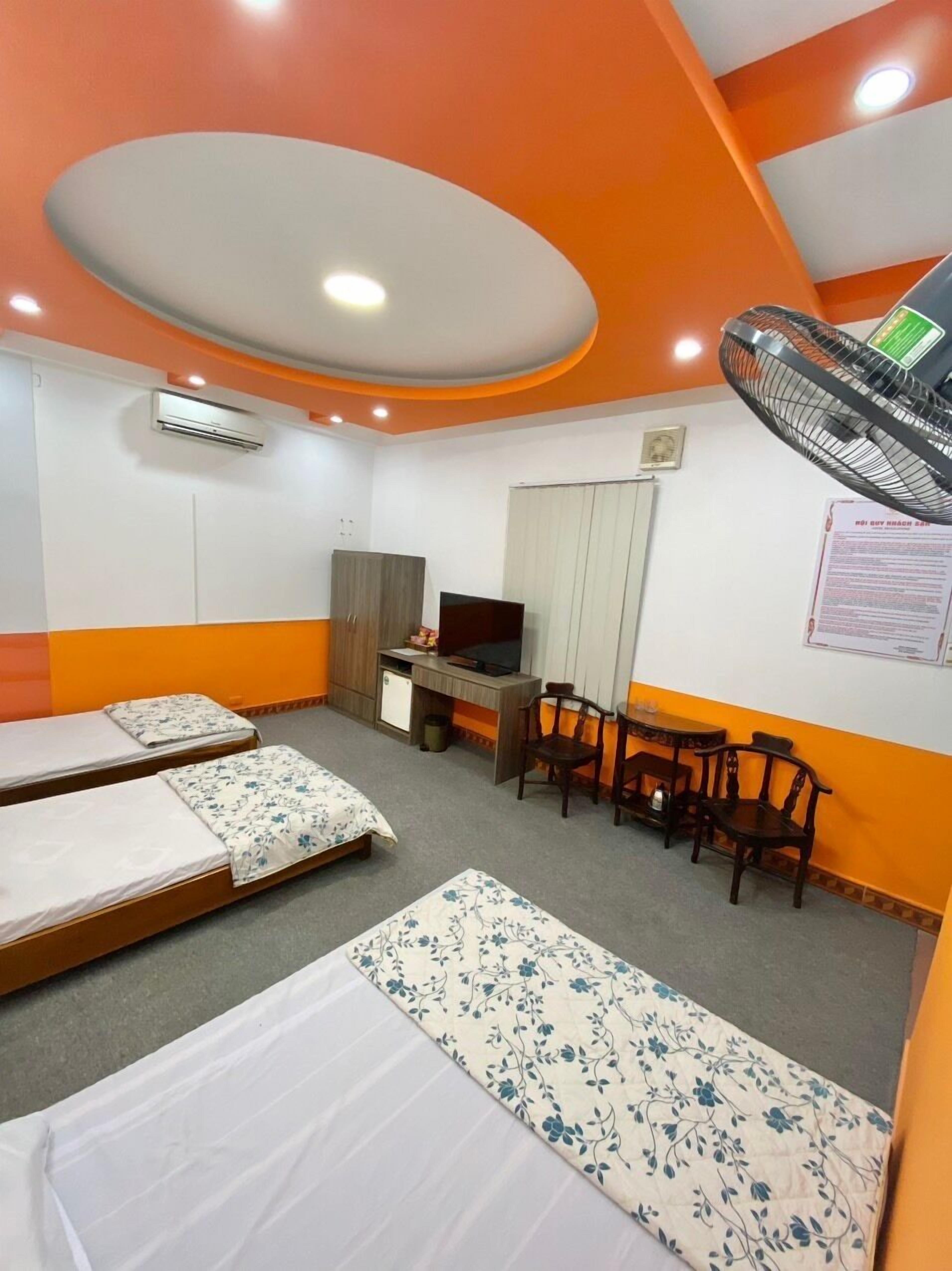 Habitación de hotel con dos camas individuales, un escritorio con silla, una mesita pequeña y un ventilador.
