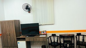 A small room with a wooden desk, a television, a refrigerator, and two chairs. - Pham Gia Hotel Ha Giang - by Bay Luxury (Ha Giang 1)
