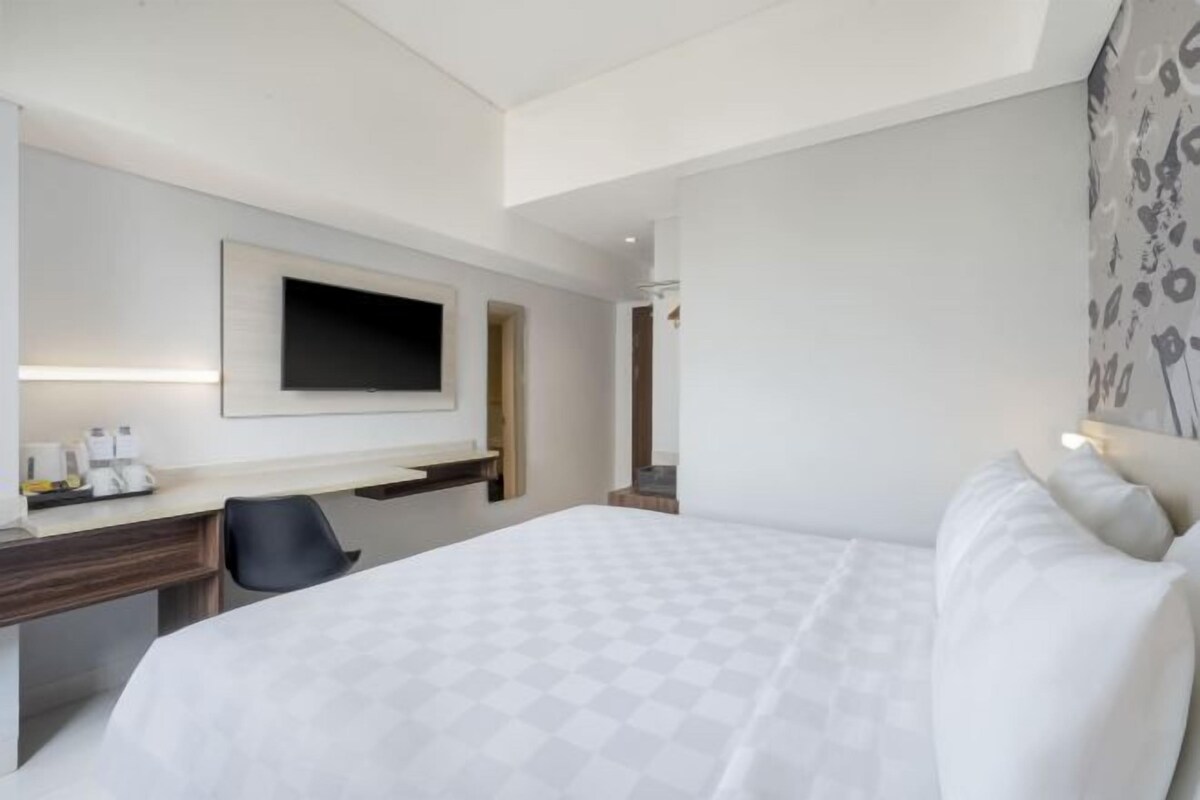 Une chambre d’hôtel comprenant un lit, un bureau, une chaise, un téléviseur à écran plat fixé au mur et un tableau accroché au mur.