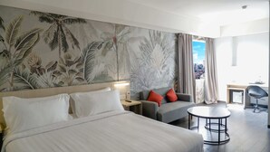 A hotel room with a large bed, a sofa, a small round table, and a view of the city through the window. - Swiss-Belexpress Cideng (Jakarta)