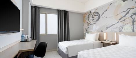 Quarto de hotel com duas camas, uma mesa, uma cadeira, televisão e janela com cortinas.