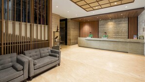 A modern reception area with a wooden reception desk, a grey sofa, and a decorative wall with vertical elements. - Swiss-Belexpress Cideng (Jakarta)