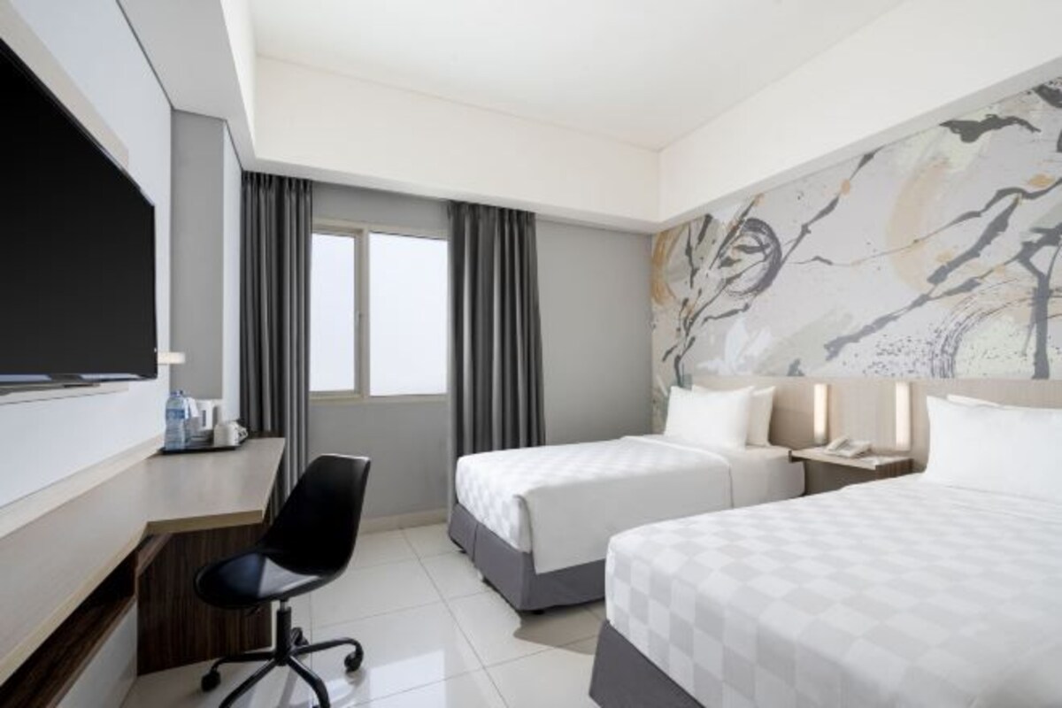 Een hotelkamer met twee bedden, een bureau met stoel, een televisie en een raam met gordijnen.