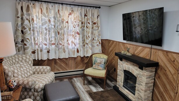 Ein Wohnzimmer mit Kamin, einem an der Wand montierten Fernseher und einem gemusterten Sofa.