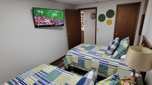 Ein Schlafzimmer mit zwei Betten, einem an der Wand montierten Fernseher und einer Lampe auf einem Holztisch.