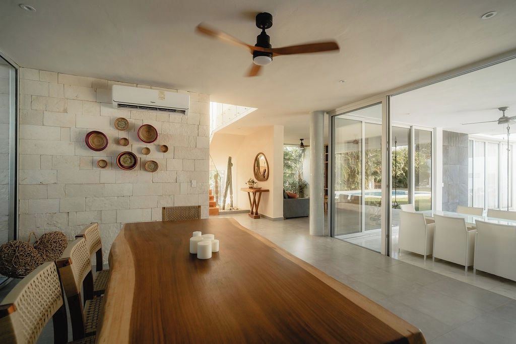 A modern dining area with a wooden table, white chairs, and a ceiling fan.