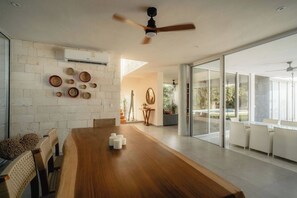 A modern dining area with a wooden table, white chairs, and a ceiling fan.