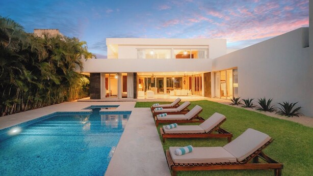 Une maison moderne dotée d’une piscine, de chaises longues et d’une pelouse bien entretenue.