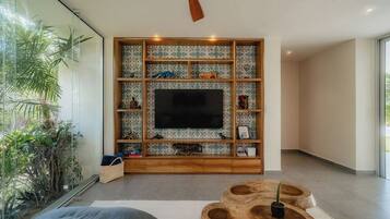 A modern living room with a large flat-screen TV, wooden shelving with decorative items, and a ceiling fan.